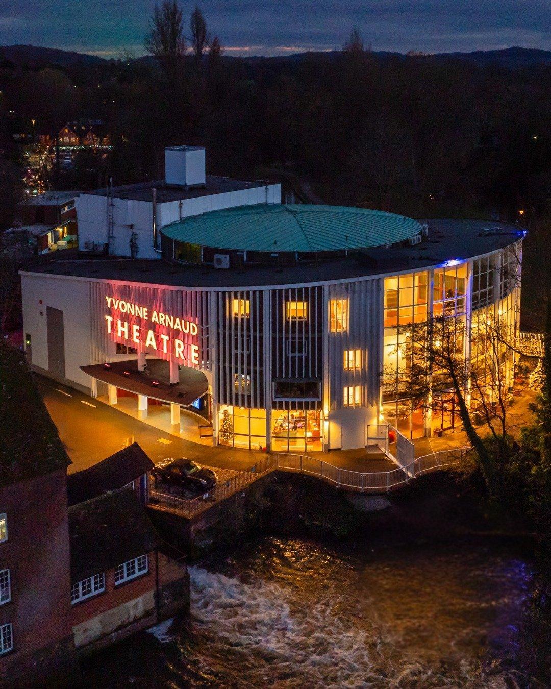 The Yvonne Arnaud Theatre in Guildford lit up at dusk beside the river.